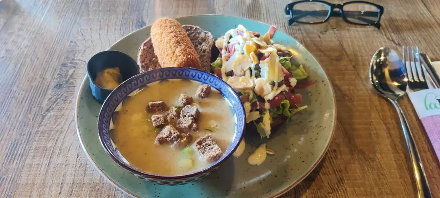 Een kom soep met croutons, een kroket en een salade op een groen bord